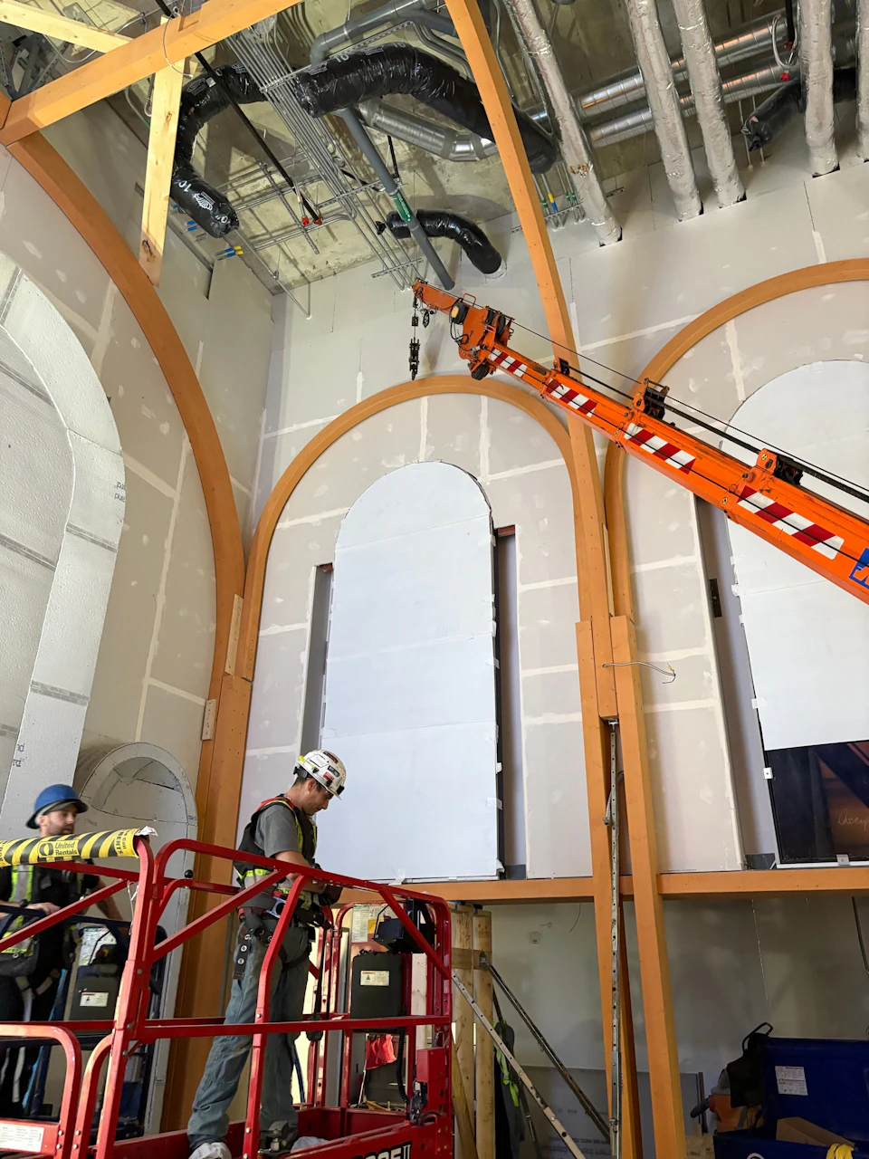 Workers on a lift beneath tall curved glulam arches inside the New St. Paul's Hospital Chapel.