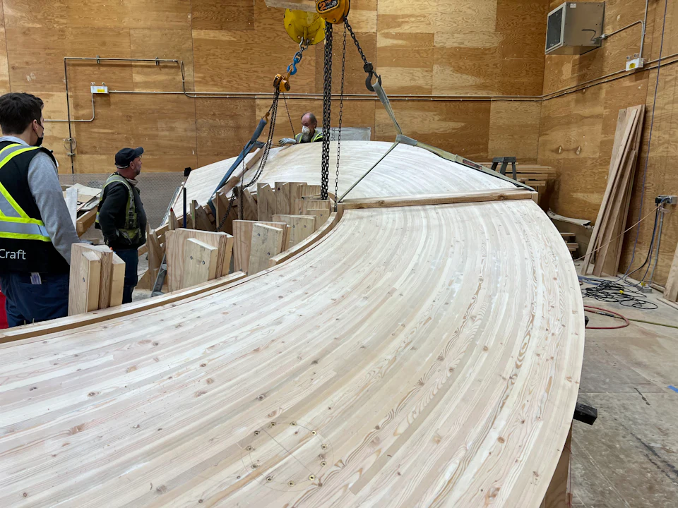 Workers lifting a curved stair stringer in the fabrication shop